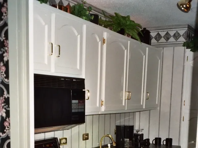 In this image we can see stove, microwave, cloth, wooden drawers, wooden cupboards, sink and cups...