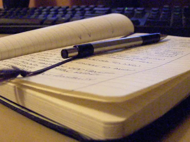 In this picture we can see a book with a pen on it, keyboard and these are placed on a table.
