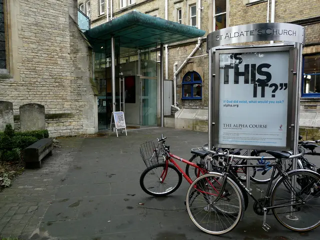 In this image there are buildings and we can see bicycles. There are boards. On the left there are...